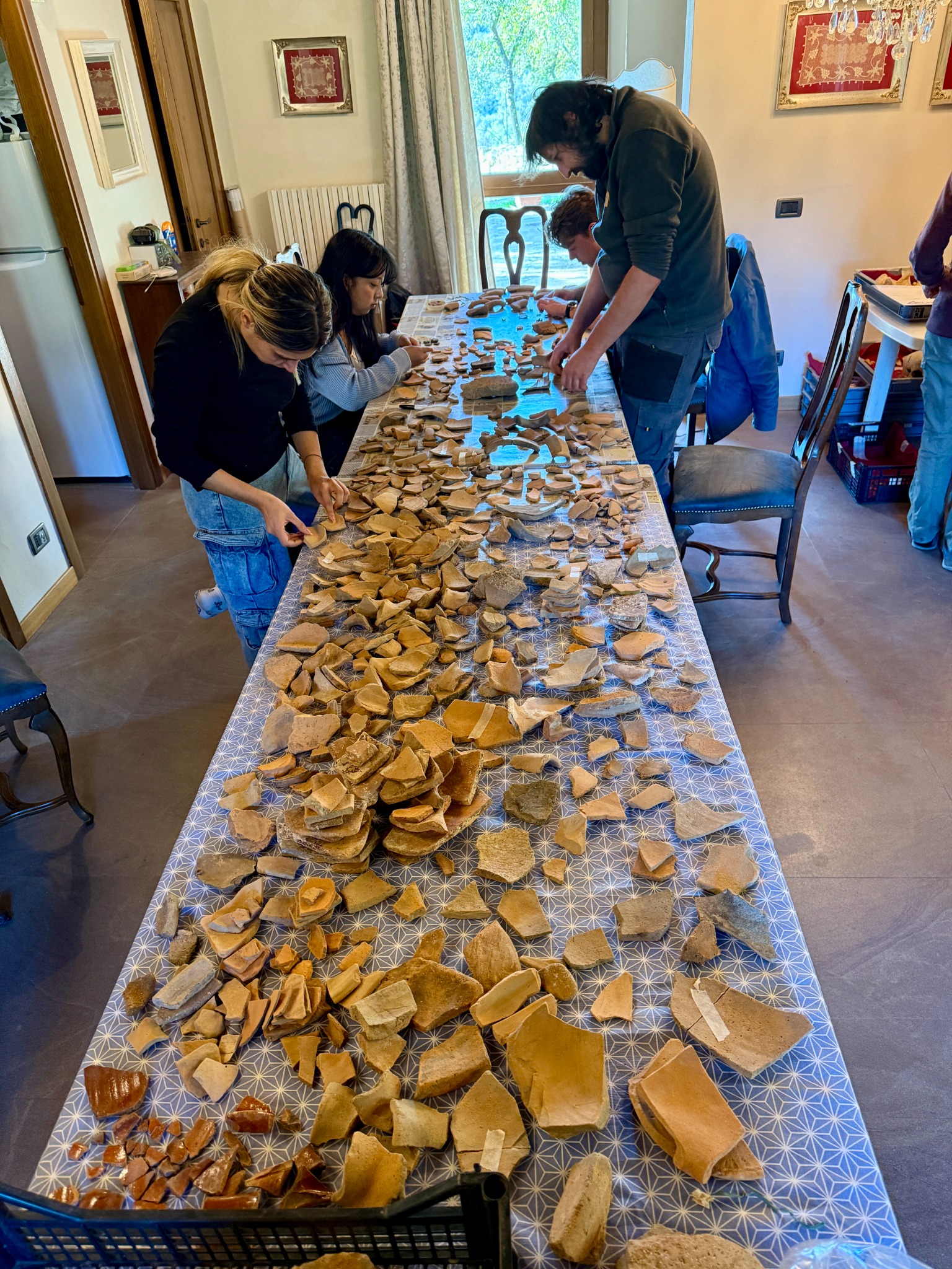 Studenti e archeologi esaminano i materiali disposti su un tavolo.
